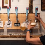 A woman, with her back to the camera, is pulling a glass of beer from a traditional beer pump.