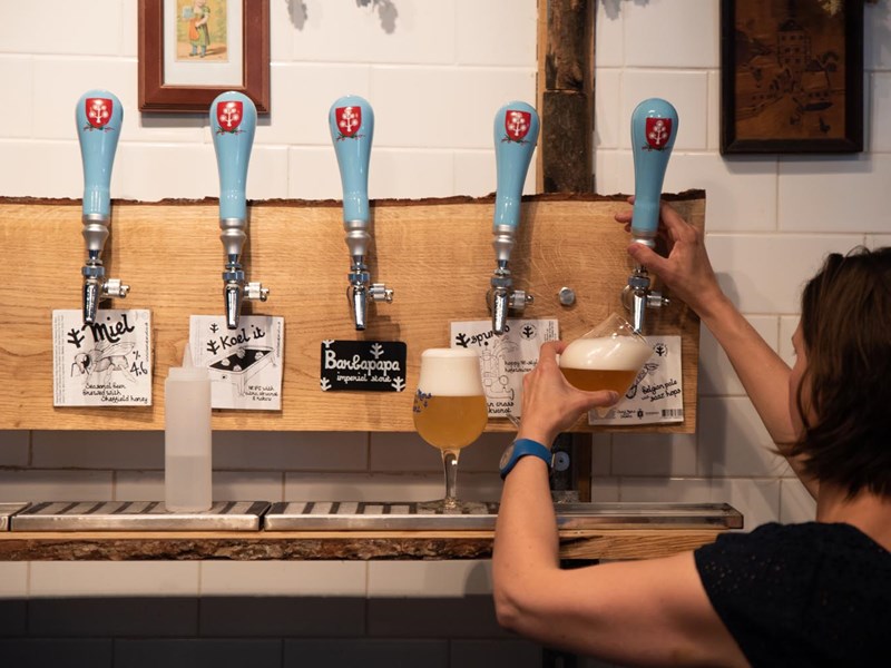A woman, with her back to the camera, is pulling a glass of beer from a traditional beer pump.