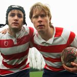 Two people in rugby gear. One of them is holding a rugby ball.