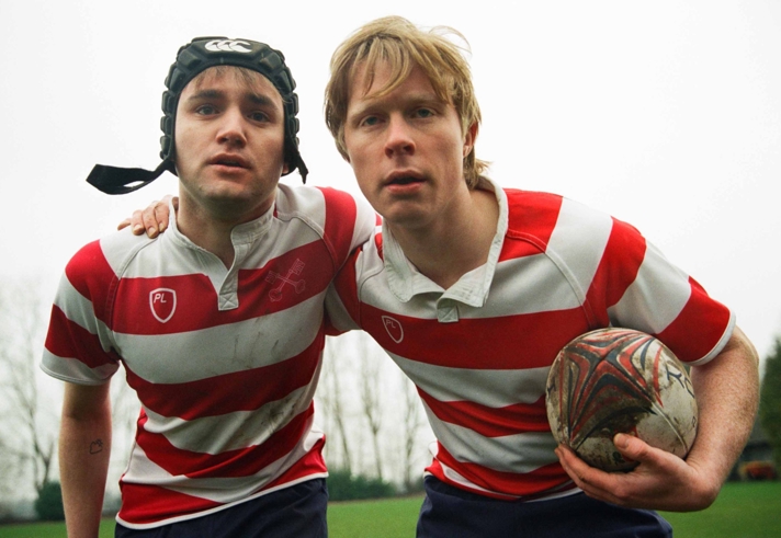 Two people in rugby gear. One of them is holding a rugby ball.