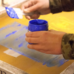 A person loading blue ink onto a printing screen.