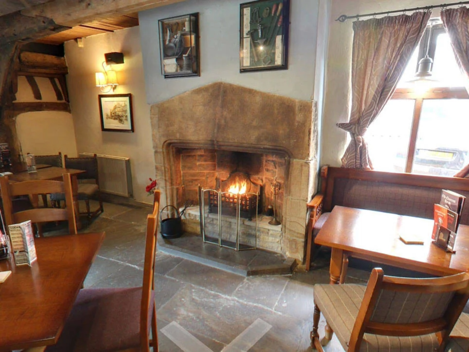 The interior of The Old Queens Head, with tables and chairs and a cosy fire place.