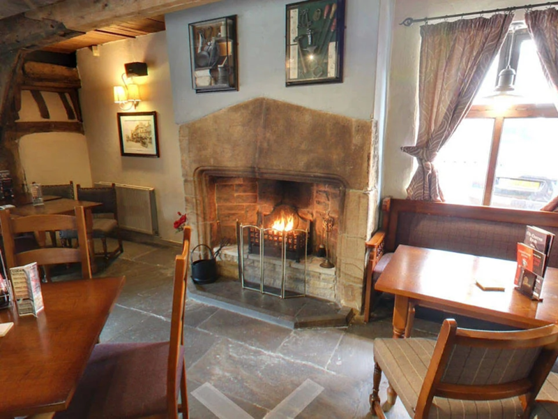 The interior of The Old Queens Head, with tables and chairs and a cosy fire place.