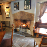 The interior of The Old Queens Head, with tables and chairs and a cosy fire place.