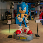 A large scale statue of the video game character Sonic the Hedgehog stands in the foreground. In the background are arcade game cabinets and other displays about video game history.