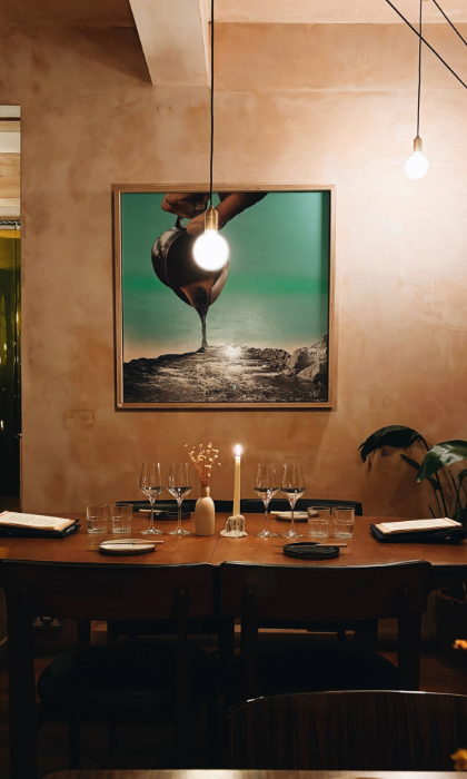 The interior of Restaurant Elm with a table laid out for two, under a large painting.