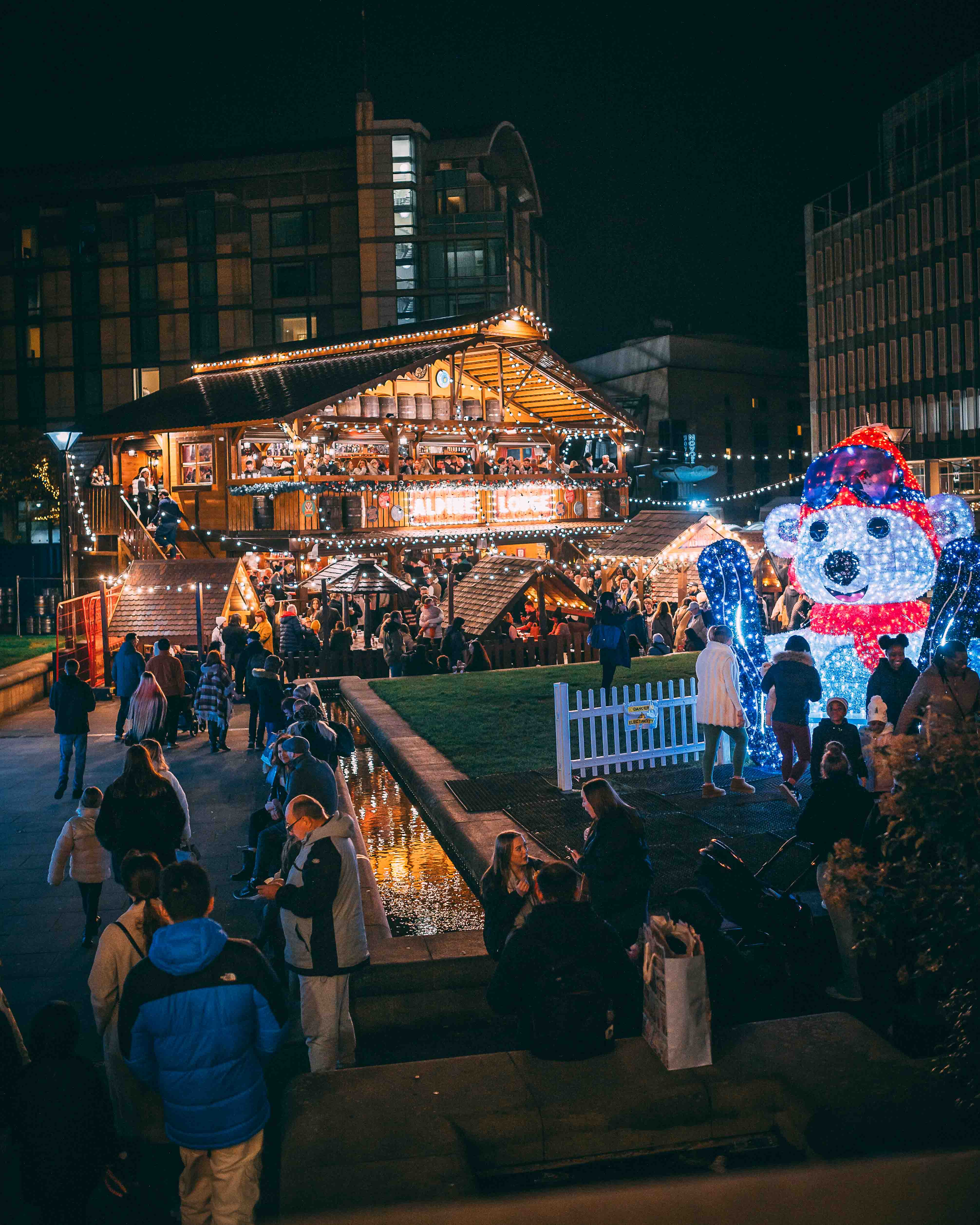 An Alpine Lodge, lit up with fairy lights, sits in the middle of the Peace Gardens as part of the Sheffield Christmas Market. In the foreground is a huge light-up polar bear.