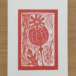 A red linocut-style print depicting a stylised seed pod with dotted detailing and a star-shaped top. A single leaf curves beside the stem. The print is framed within a textured rectangular border on white paper.