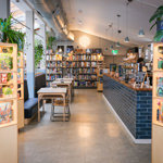 Inside The Treehouse Cafe. You can see tables and chairs, the counter and three shelving units full of board games.
