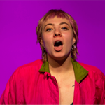 A woman with a pink shirt has her mouth open as if shouting or singing.