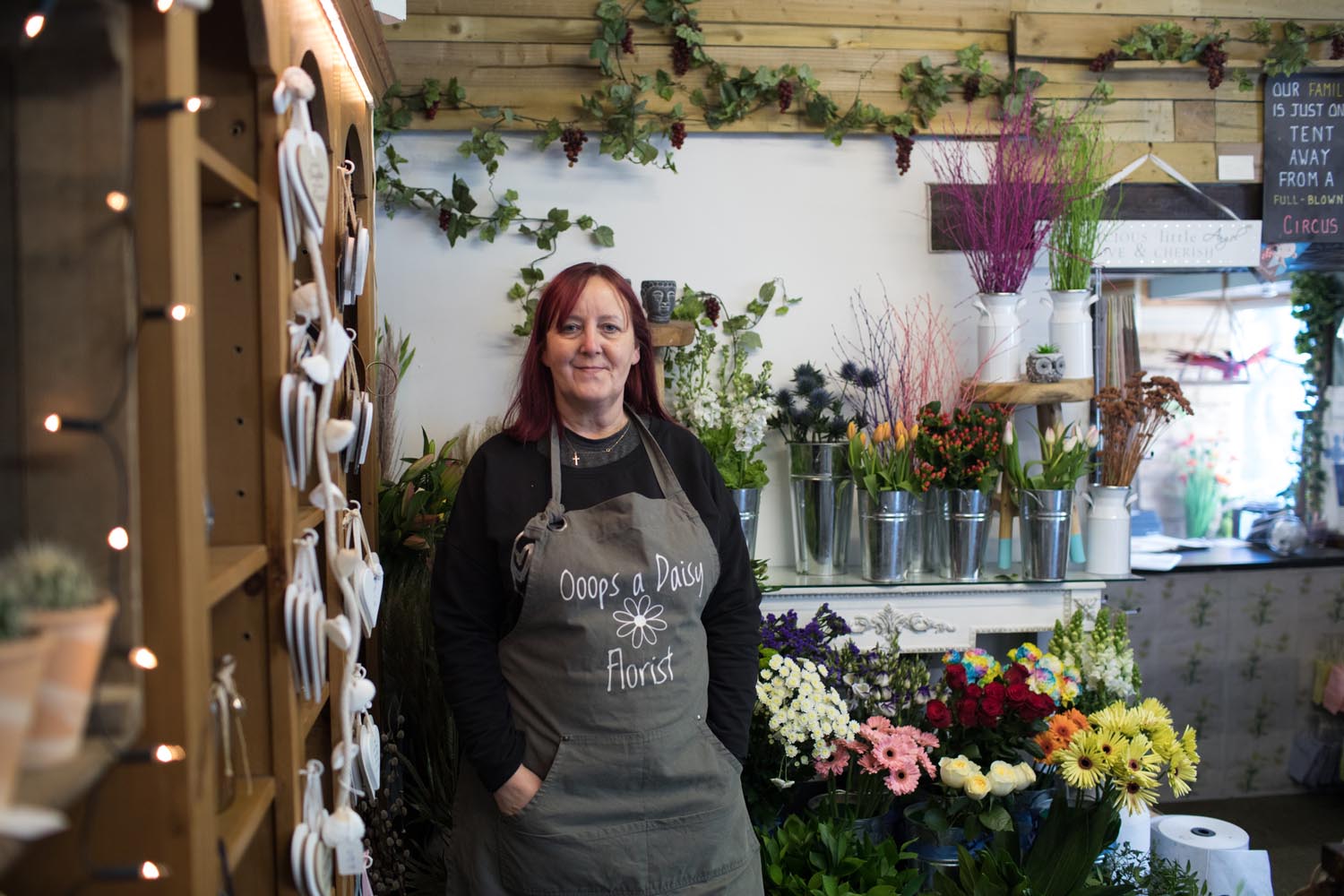 A Sheffield florist stands in front of rows of many vases of flowers of all colours.