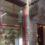 Exterior of a brick‑fronted shop with a red‑framed window displaying ceramics, and a hanging sign reading “Earth Paper Fibre” above the entrance.