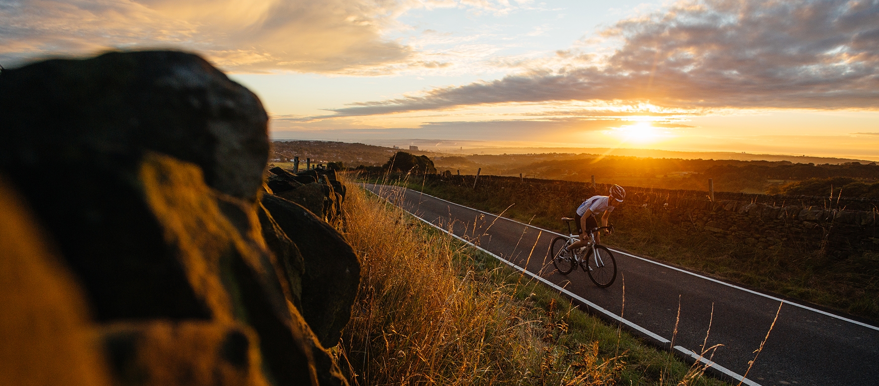 Cyclist riding along countryside road while the sun sets in the background.