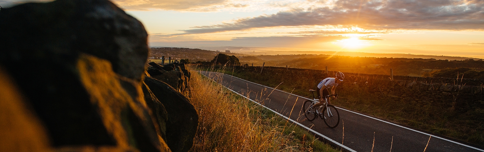Cyclist riding along countryside road while the sun sets in the background.