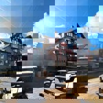 A sunlit outdoor decking area behind The Punch Bowl, with wooden picnic tables and string lights, and the pub building visible in the background.