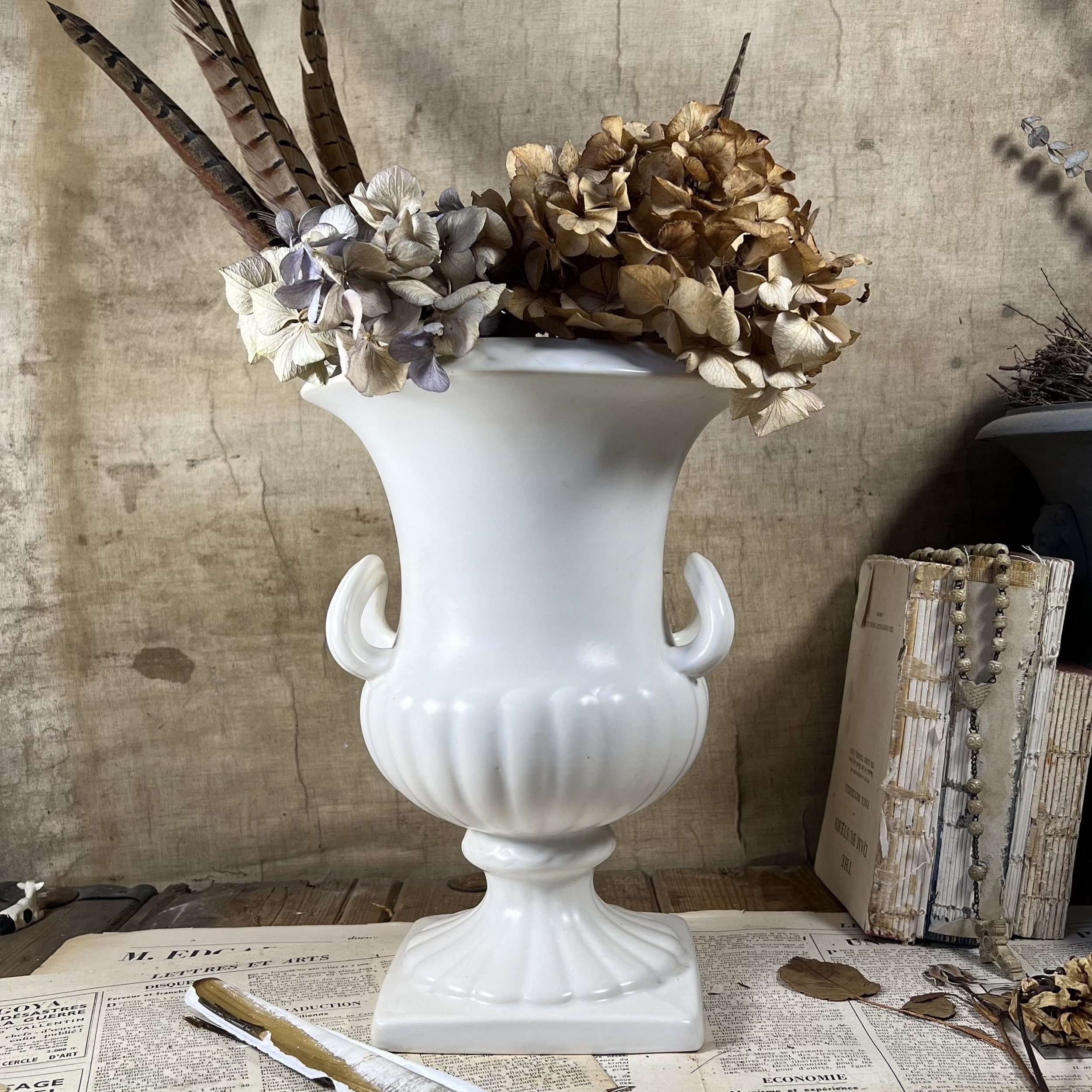 A white porcelain vase, in the style of a Greek urn, with dried flowers in.