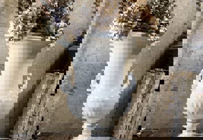 A white porcelain vase, in the style of a Greek urn, with dried flowers in.