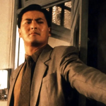A still from a film with Chow Yun Fat flat against a wall holding a gun.