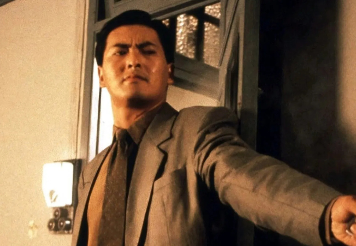 A still from a film with Chow Yun Fat flat against a wall holding a gun.
