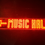 A red neon sign that reads 'Music Hall' with an arrow pointing left.