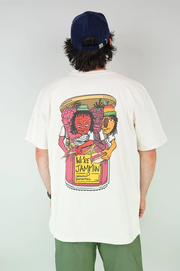A man stands with his back to the camera, wearing a baseball bat, a white t-shirt with a colourful back print and green trousers. The design on the shirt is four anthropomorphic fruits busting out of a jam jar. They look like members of a band. The yellow label on the jar reads 'We're jammin''.