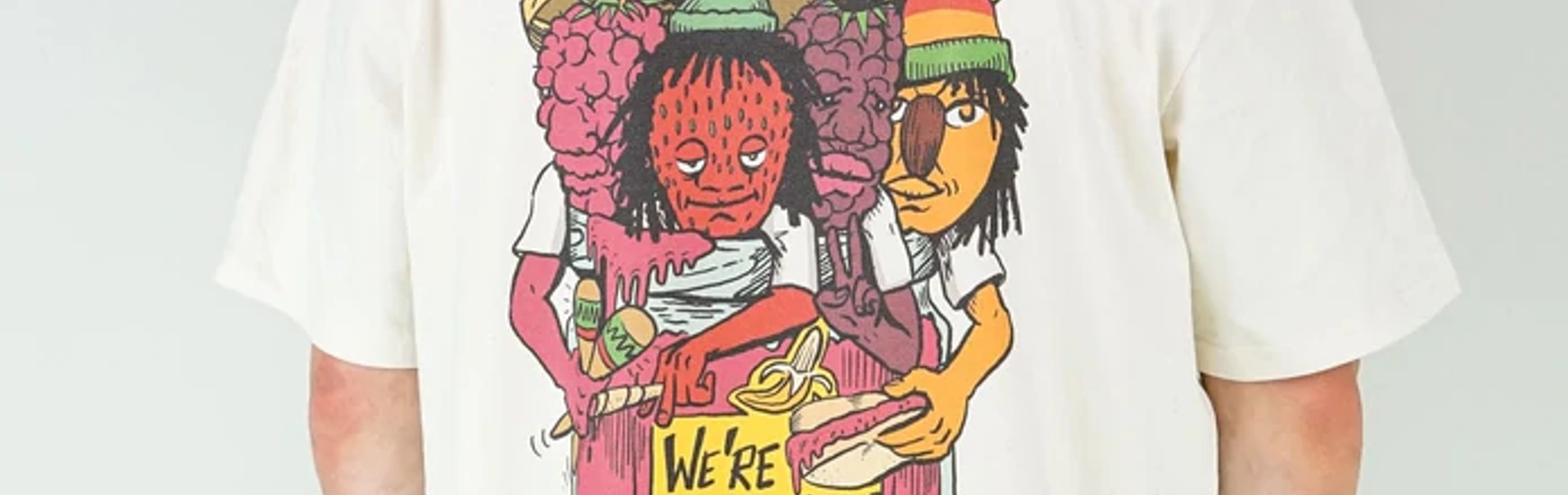 A man stands with his back to the camera, wearing a baseball bat, a white t-shirt with a colourful back print and green trousers. The design on the shirt is four anthropomorphic fruits busting out of a jam jar. They look like members of a band. The yellow label on the jar reads 'We're jammin''.