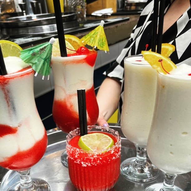 Five cocktails being carried on a metal tray.