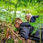 Two children, with face-paint on, are creeping through the undergrowth at TRIBE Bushcraft Centre