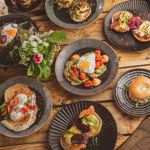 Eight different dishes laid out on a wooden table.