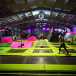 A huge room full of multiple trampolines, filled with adults and children having fun.