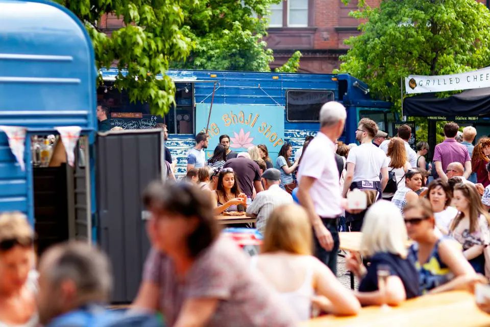 People sit surrounded by street food stands on a sunny day 
