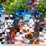 People sit surrounded by street food stands on a sunny day 