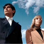 A picture of the band, which consists of two individuals, each one of them is looking into a different direction, with wind blowing on them