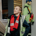 A boy dressing up in a high-vis vest and a life jacket.