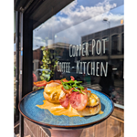 Eggs Benedict with bacon, on a blue plate, being held up outside the Copper Pot Café.