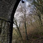 A tall stone arch of a bridge over a river. A person is abseiling down the side.