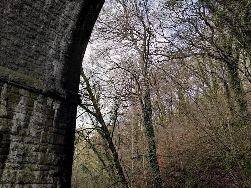 A tall stone arch of a bridge over a river. A person is abseiling down the side.