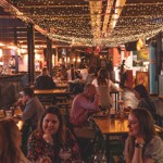 A view inside Cutlery Works: there are people sat at tables eating, chatting and having a good time. The ceiling is festooned with twinkling fairy lights. 