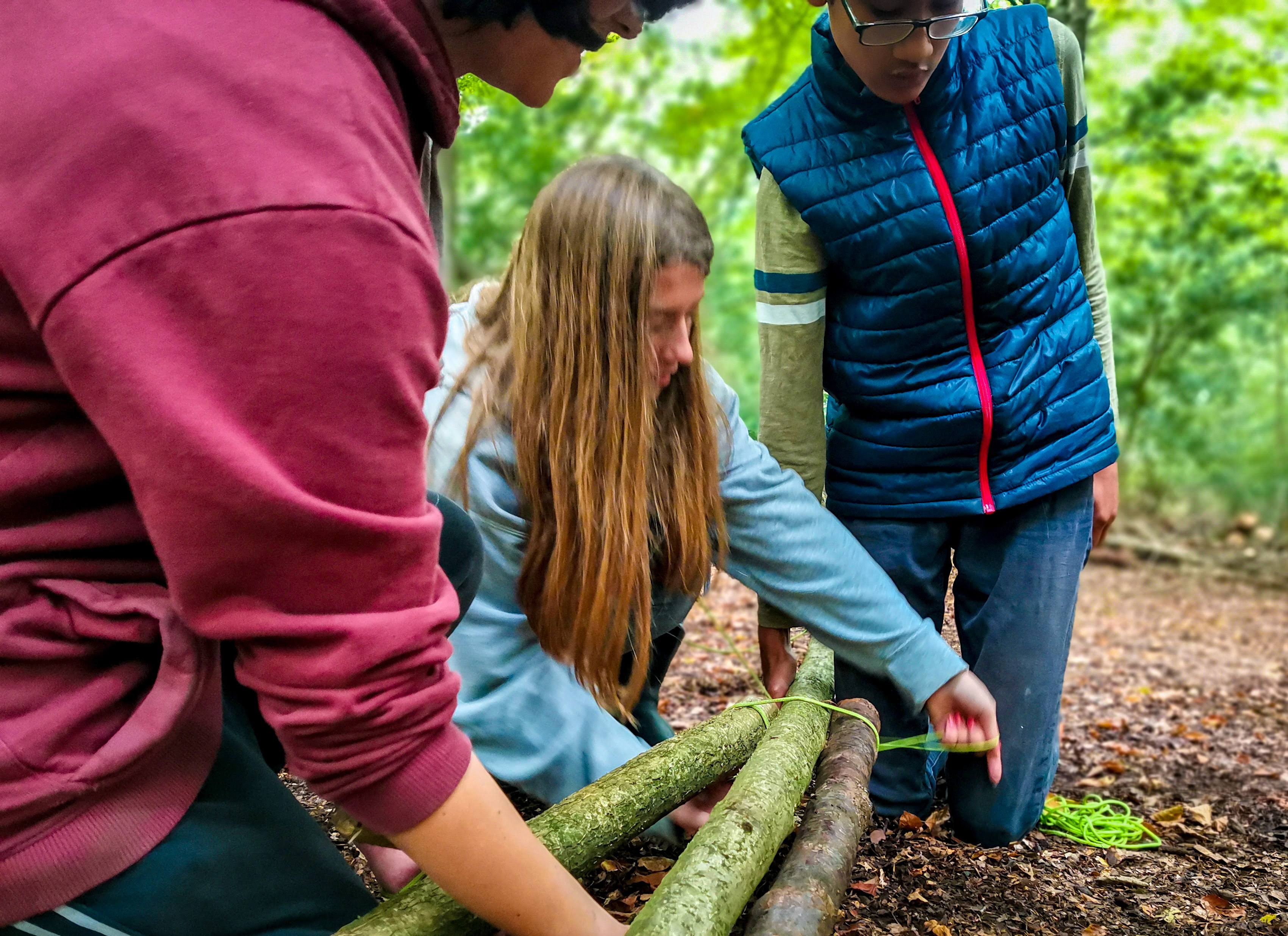 People are tying three logs together with strong twine at the TRIBE Bushcraft Centre