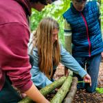 People are tying three logs together with strong twine at the TRIBE Bushcraft Centre