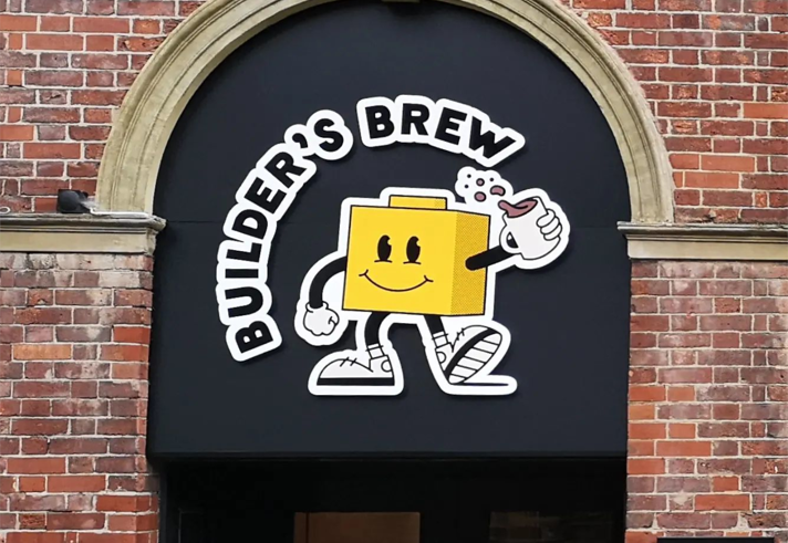 Builder's Brew Café logo on the outside of a building. The logo has the words 'Builder's Brew' round a cartoon character, who is shaped like a toy building brick, holding a mug of tea.