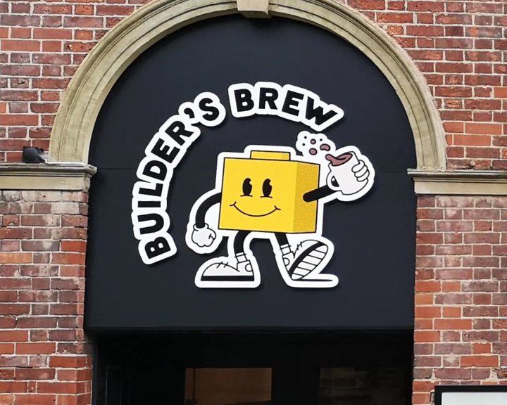 Builder's Brew Café logo on the outside of a building. The logo has the words 'Builder's Brew' round a cartoon character, who is shaped like a toy building brick, holding a mug of tea.