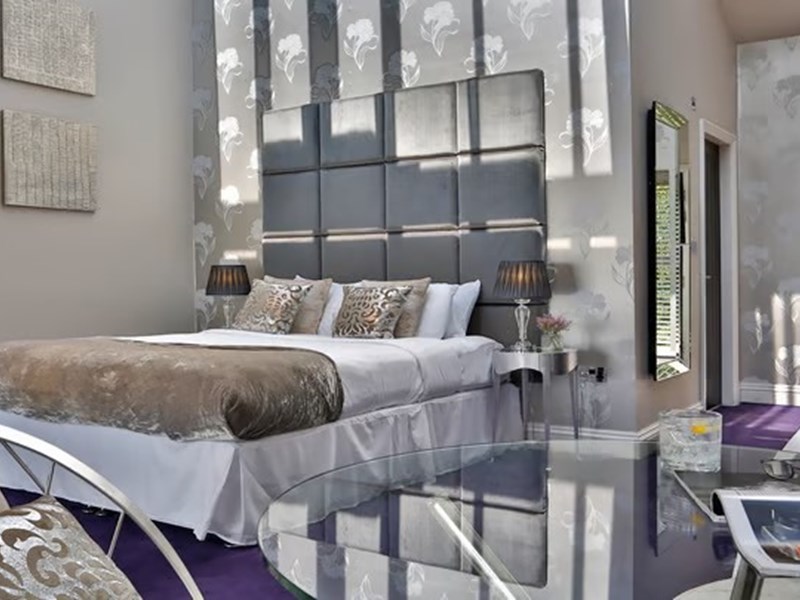 Opulent hotel bedroom at Aston Hall Hotel with king-size bed, cushions, and warm lighting creating a relaxing ambiance.