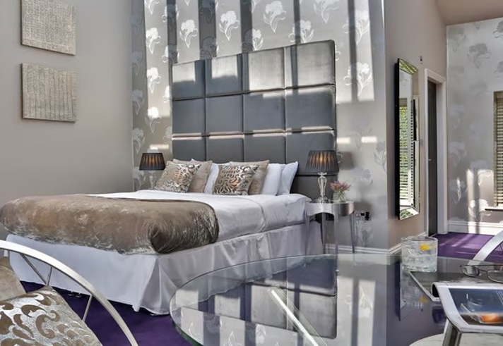 Opulent hotel bedroom at Aston Hall Hotel with king-size bed, cushions, and warm lighting creating a relaxing ambiance.