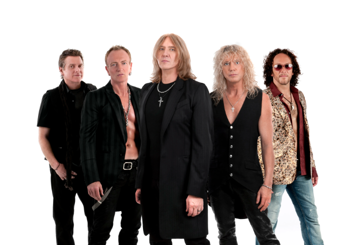 Five people standing together in a studio setting, dressed in rock-style outfits. Clothing includes black leather pants, open shirts, long coats, and patterned vests. Several wear necklaces with cross pendants. The background is plain white, and the group is posed in a staggered formation.
