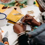 A close-up of two people sat at a table, sewing.