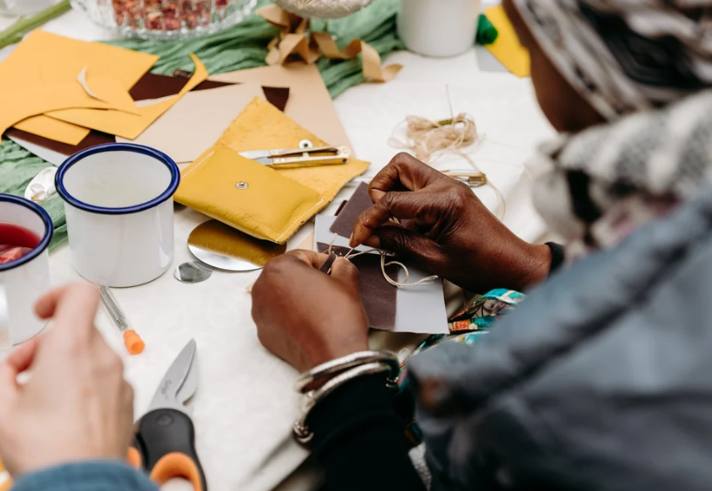 A close-up of two people sat at a table, sewing.