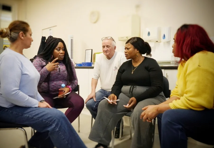 Five people, sat on chairs, are having a discussion.