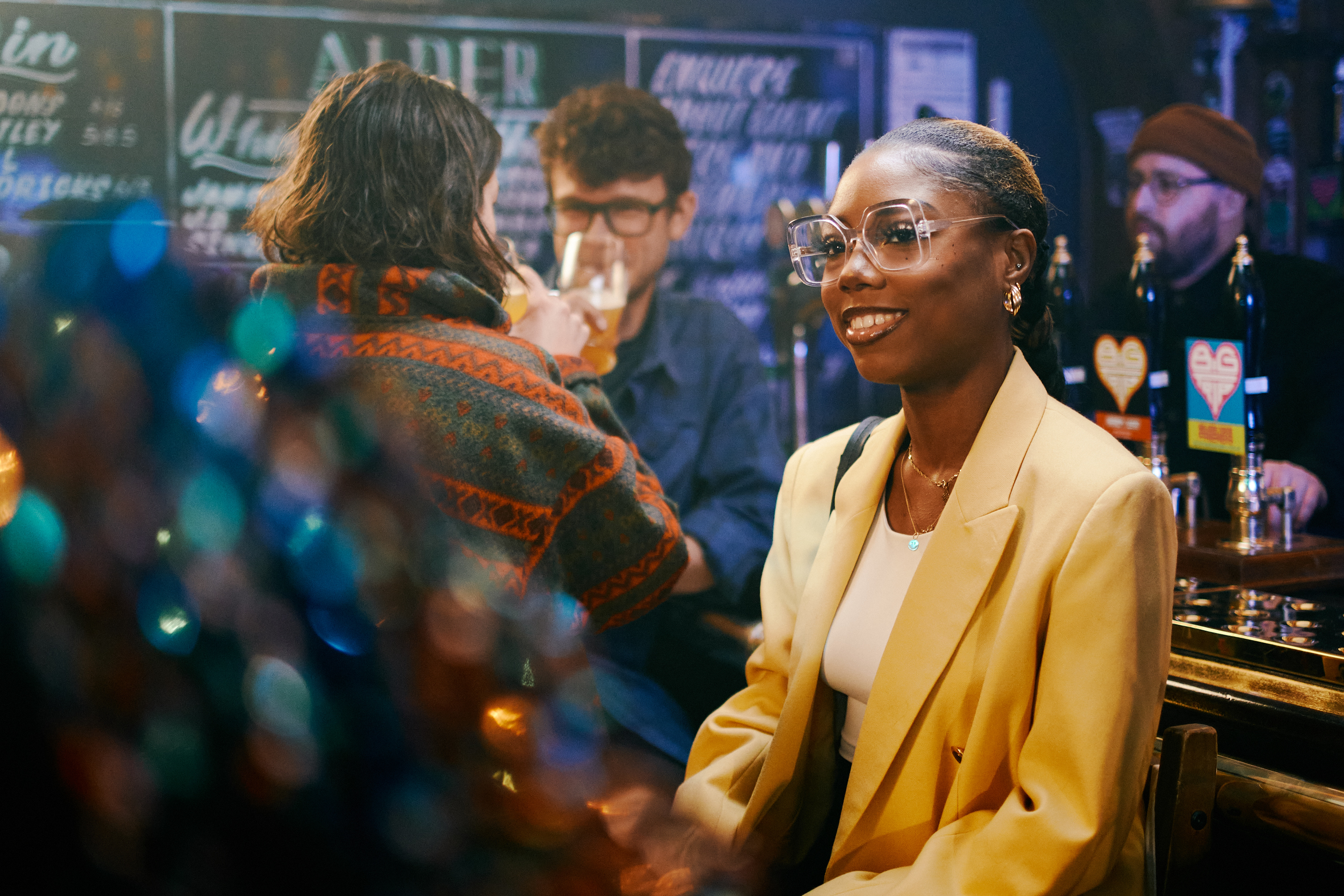 A group of people enjoying at night out, sat at the bar in a pub.
