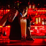 A man mixing a cocktail in a bar that has subdued red lighting.